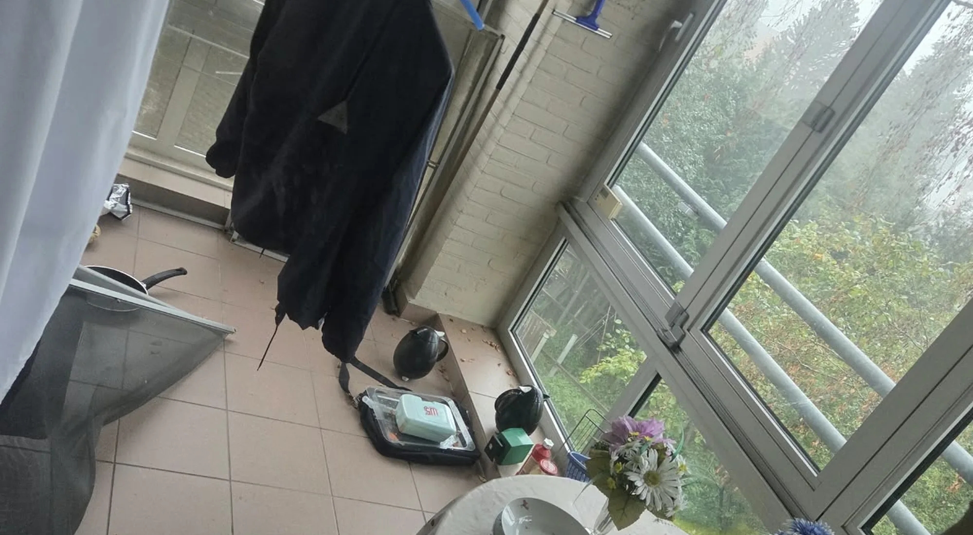 Appartement leegmaken: veranda met kledingrek en losse spullen op de tegelvloer