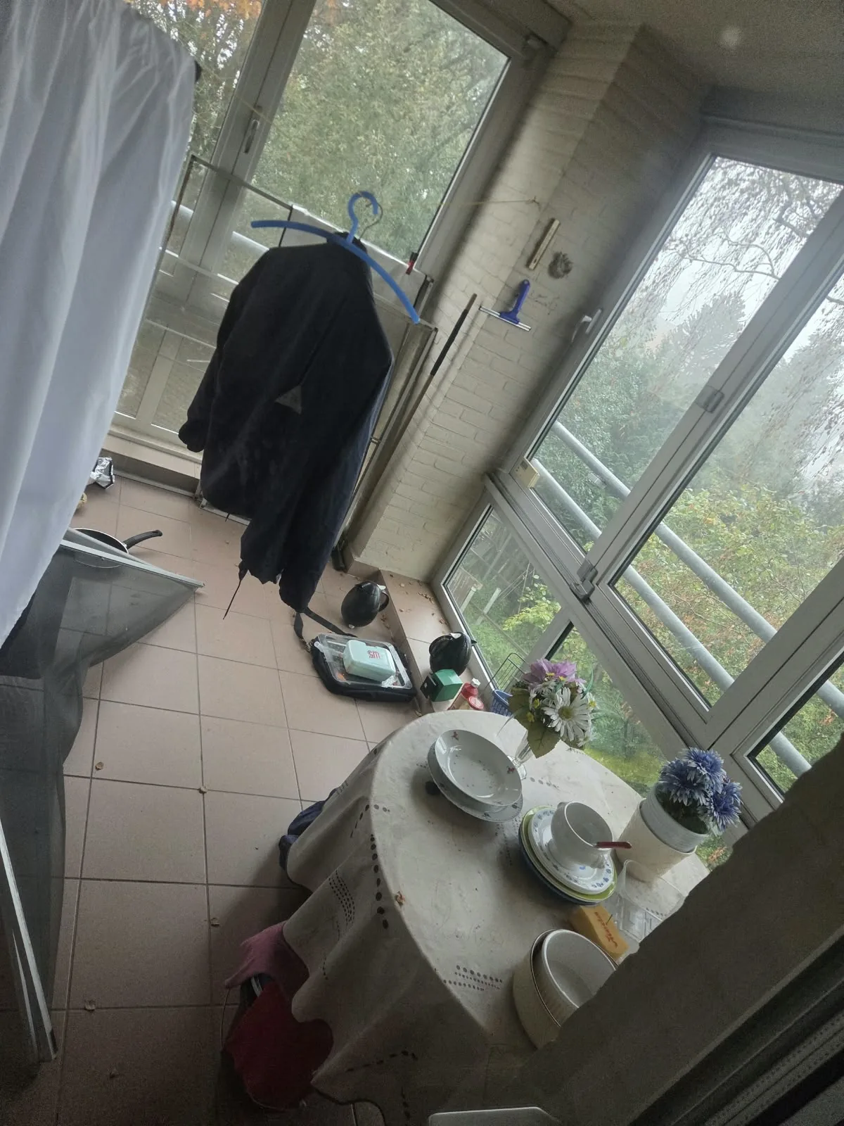 Appartement leegmaken: veranda met kledingrek en losse spullen op de tegelvloer